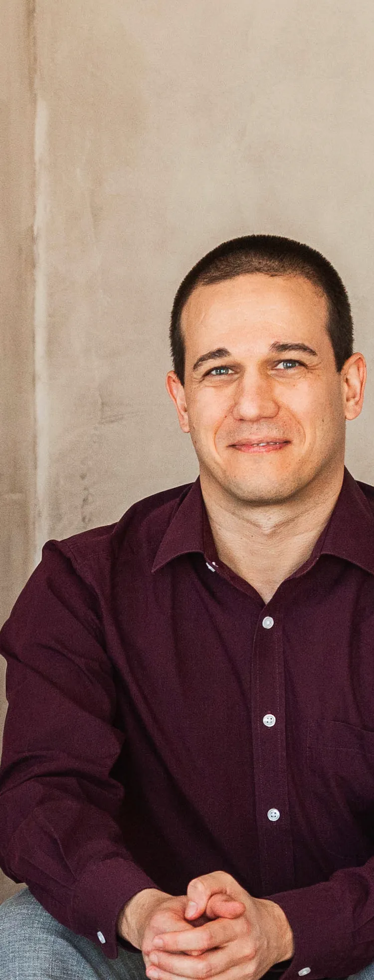 Csordás Péter egy fából készült ülőkén ül, nyers betonfal előtt