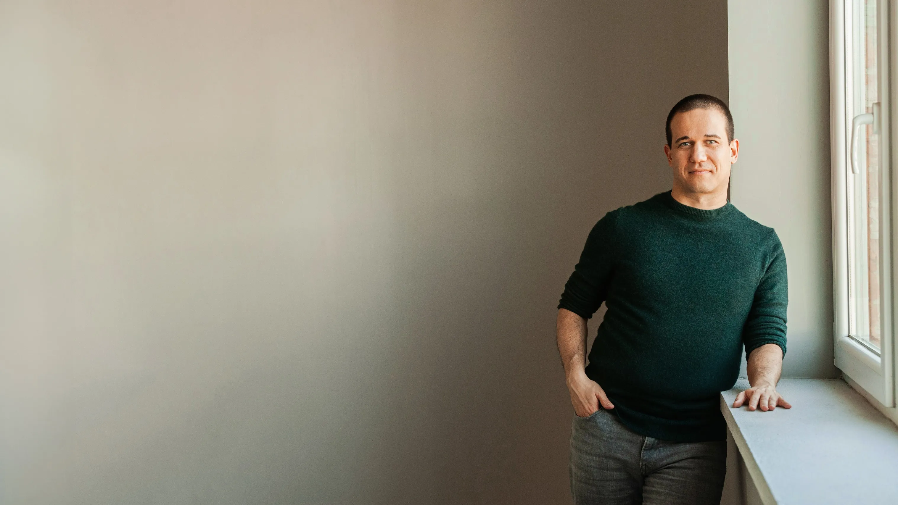 Csordás Péter egy ablak mellett áll, kezét a párkányon nyugtatva